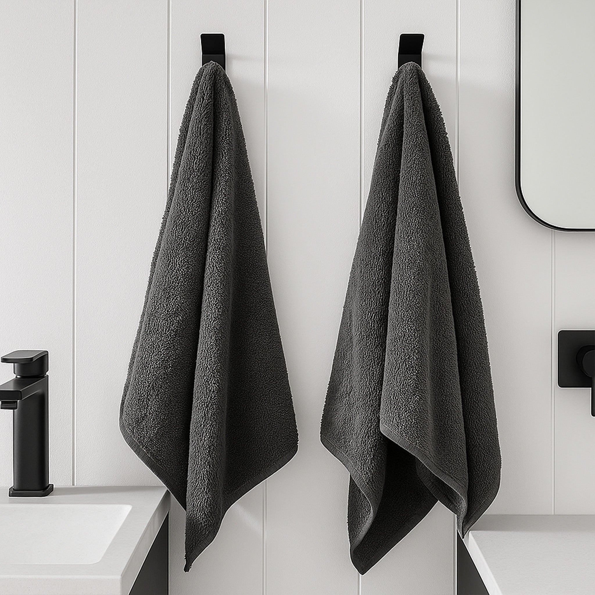 Set of 2 minimalist stainless steel wall hooks holding dark gray towels in a modern bathroom setting